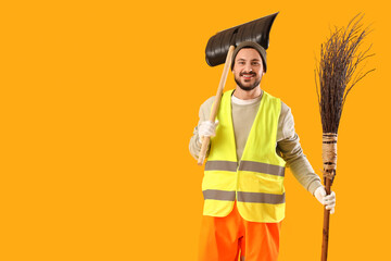 Male scavenger with snow shovel and broom on yellow background
