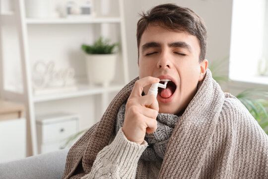Ill young man with plaid spraying his sore throat at home, closeup