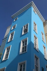 A blue-painted building with white windows, viewed from the corner, against a clear blue sky on a sunny day