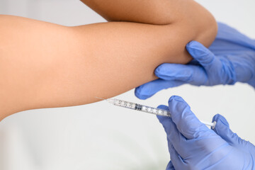 Young woman receiving injection in her arm at cosmetologist's office, back view