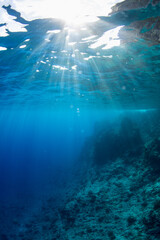 Sun rays through the clear blue waters off the coast of Orote Point, Guam, showing the descending reef wall 