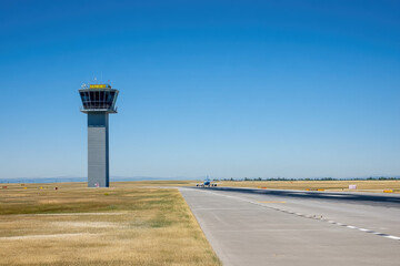 Airplane taxiing on the runway, with airport control tower in view. Copyspace on the left. Bright, sunny lighting. Clear blue sky and runway background.