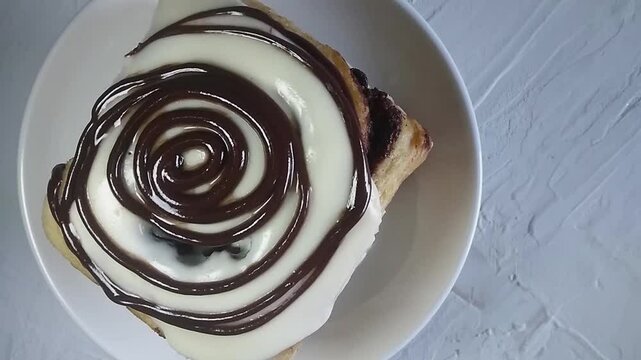 Frosted Cinnamon Roll on White Plate with Chocolate Topping