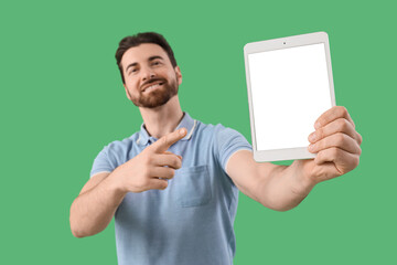 Handsome man pointing at blank tablet computer on green background