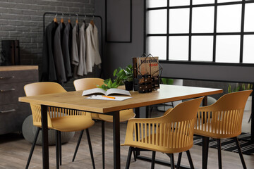 Stand with magazines and plant on table in clothing store office