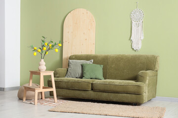 Interior of living room with green sofa, tree branches and lemons in vase