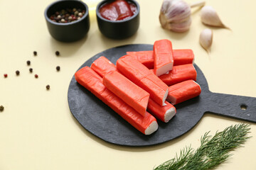 Black board with tasty crab sticks and different spices on yellow background © Pixel-Shot