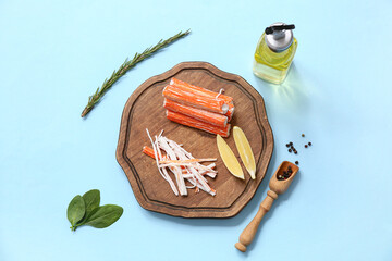 Wooden board with tasty crab sticks, pieces of lemon and rosemary on blue background © Pixel-Shot