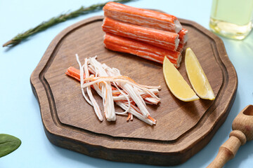 Wooden board with tasty crab sticks, pieces of lemon and rosemary on blue background © Pixel-Shot