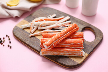 Wooden board with tasty crab sticks and peppercorns on pink background © Pixel-Shot