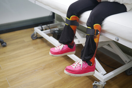 Child's Legs With Orthopedic Braces and Bright Pink Shoes on Clinic Bed