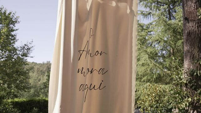 Decorative banner reading "O Amor mora aqui" in a sunny outdoor setting with trees