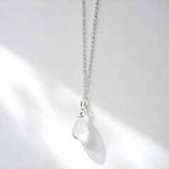 Minimalist silver necklace with tear drop pendant captured in soft light, photography of still life concept.