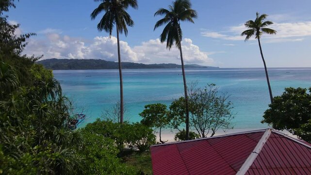 A Red-roofed Structure Overlooks Turquoise Waters and Palm Trees in Sulawesi, Indonesia - Drone Flying Forward