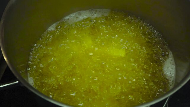 Close up or closeup footage of home made golden yellow french fries cooking in vibrant bubbly and hot oil that is bubbling and foaming in slow motion in a metallic gray pot on a stove indoors.