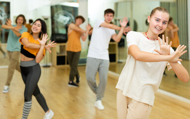 Group of active teens rehearsing modern dance in studio.