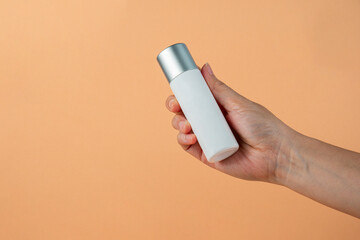 White cosmetic bottle in hand, Skin care or sunscreen cosmetic on cream background