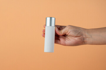 White cosmetic bottle in hand, Skin care or sunscreen cosmetic on cream background