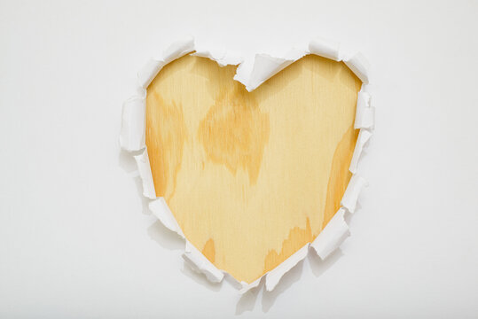 Heart-shaped hole torn in the center on white paper revealing a wooden background - Powered by Adobe