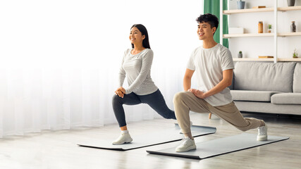 Fototapeta premium Motivated asian young couple exercising together at home, positive korean man and woman in sportswear standing on fitness mat, stretching and smiling, copy space. Healthy lifestyle concept