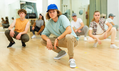 Group of teenagers squatting during group rehearsal of hip-hop dance.