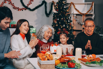 Multi-Generation Family Celebrate Christmas At Home Wearing Santa Hats And Antlers Opening Presents