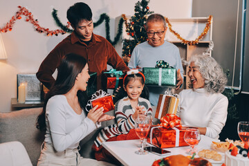 Portrait of Asian family exchanging presents during christmas at home. Attractive happy people holding gift box, celebrate holiday thanksgiving, xmas eve tradition in living room in house together.