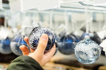 A man chooses white Christmas balls in a store against a blurred background. Christmas shopping concept