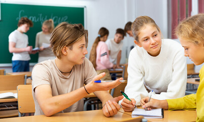 Fototapeta premium Teenage schoolchilds working in groups at lesson in secondary school with teacher on background
