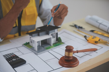 Judge gavel on building blueprint plans with a yellow safety helmet in the background. law that deals with matters relating to building construction, engineering. Construction law concept.