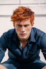 Headshot of red haired serious young male, dressed casually, with blue denim, isolated over white background
