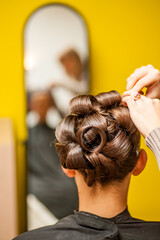 Fototapeta premium A stylist is meticulously creating an elegant updo hairstyle in a vibrant and lively salon environment