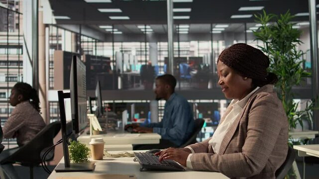 Focused african american general manager multitasking at desk to solve business tasks and operations on computer and documents. Woman meeting deadlines while making strategic decisions. Camera B.