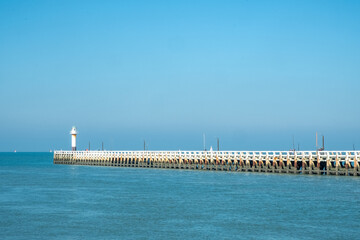 A picturesque pier extends into the ocean, with a lighthouse beneath sunny skies, creating an...