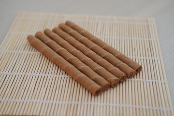 Six chocolate wafer rolls are neatly arranged in a row on a bamboo mat