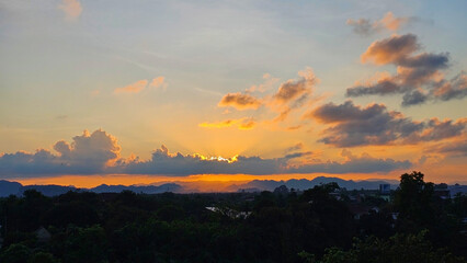 Serene sunset over a tranquil landscape, showcasing vibrant hues painting the sky. Clouds glow with warm light, casting a peaceful atmosphere. 