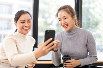 Two happy and excited young girls using mobile phones while sitting at the cafe, talking together and laughter.