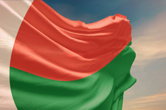 Waving flag of Madagascar in blue sky. Madagascar flag on pole for Independence Day. The symbol of the state on wavy fabric.