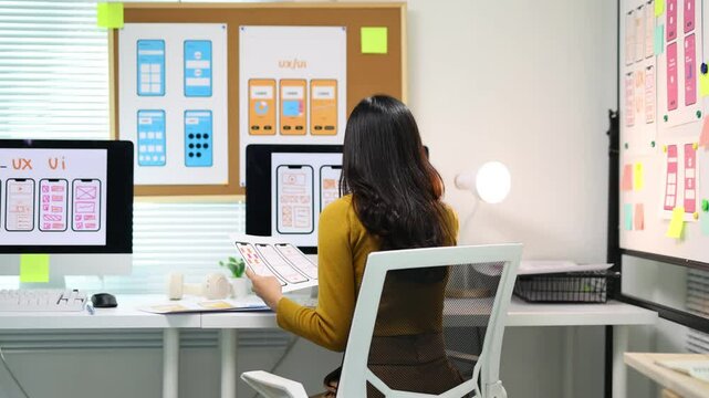 Female ui ux designer working on mobile app design prototype. Ui/ux designer is analyzing the user flow of a mobile application prototype she is designing, using sticky notes on a whiteboard.