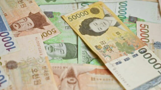 South korean banknotes, including denominations of 50000, 10000, and 5000 won, displayed in a scattered arrangement highlighting various designs and portraits, emphasizing local currency.