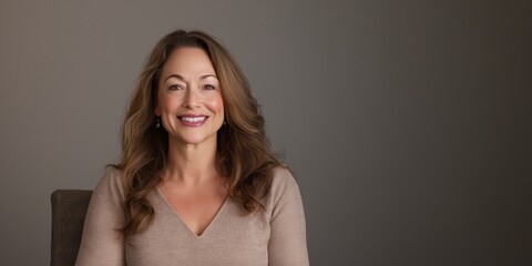 A confident woman sitting elegantly on a chair, smiling warmly against a neutral backdrop, exemplifying grace and self-assuredness in professional and social settings.