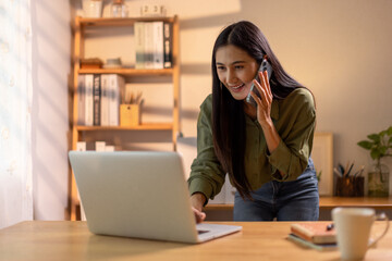 Beautiful young Asian woman working with laptop computer in home kitchen. Work at home. Remote studying E-learning, Watching online education, Webinar at house
