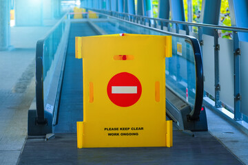 Yellow fence with a brick sign, passage is prohibited on a travellator, an elevated pedestrian...