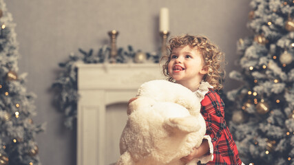 Kleines hübsches Mädchen mit Weihnachtskleidung und Teddybär in Weihnachtskulisse und Kamin Var. 5