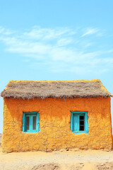 Colorful mud house with thatched roof under clear blue sky in a rural setting