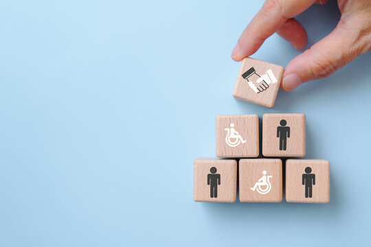 For supported employment and inclusive workplace concept. wooden cube blocks with disabled person and men icons, hand place handshake sign on top on blue background