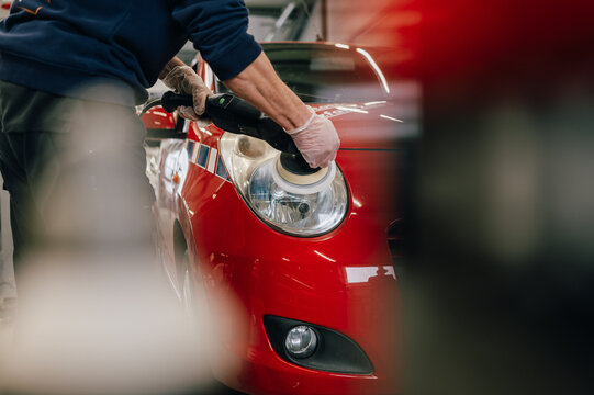 Ein Autopflege-Spezialist poliert den Scheinwerfer eines roten Autos mit einer professionellen Poliermaschine. Die Szene zeigt die Pr&auml;zision und Detailarbeit bei der Fahrzeugaufbereitung.