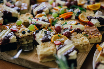 Ein Buffet mit einer Vielzahl von Kuchenstücken, dekoriert mit frischen Früchten wie Trauben, Orangen und Beeren. Die bunte und detailreiche Präsentation wirkt einladend und appetitlich.