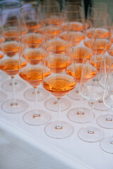 Eine elegante Anordnung von Weingläsern, gefüllt mit einem leuchtend orangefarbenen Aperitif, auf einem weiß gedeckten Tisch. Die Szene wirkt festlich und stilvoll, passend für einen Empfang.