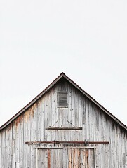 A weathered barn rises under a clear sky, adorned with rustic wood and metal, complemented by farming tools leaning against it, ideal for agricultural-themed imagery.